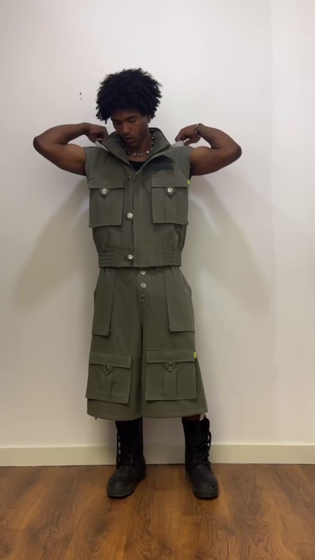 Model wearing Days Of War olive green cargo set: sleeveless hooded vest with white-lined hood and multiple pockets, paired with a long cargo short and black combat boots